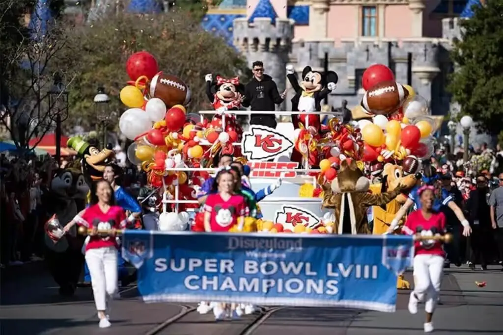 Patrick Mahomes celebrates the Kansas City Chiefs’ Super Bowl LVIII victory during a festive Disneyland parade on Main Street, surrounded by Mickey, Minnie, Goofy, and colorful football-themed balloons.
