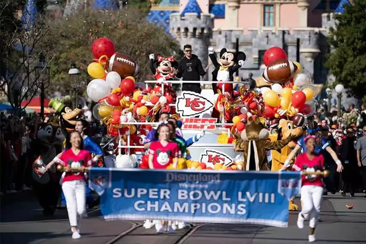 Patrick Mahomes celebrates the Kansas City Chiefs’ Super Bowl LVIII victory during a festive Disneyland parade on Main Street, surrounded by Mickey, Minnie, Goofy, and colorful football-themed balloons.