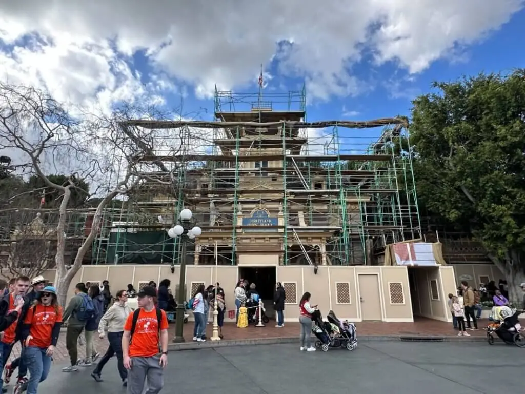 Disneyland City Hall under refurbishment with scaffolding and construction walls, illustrating theme park maintenance and updates as guests walk through Town Square.