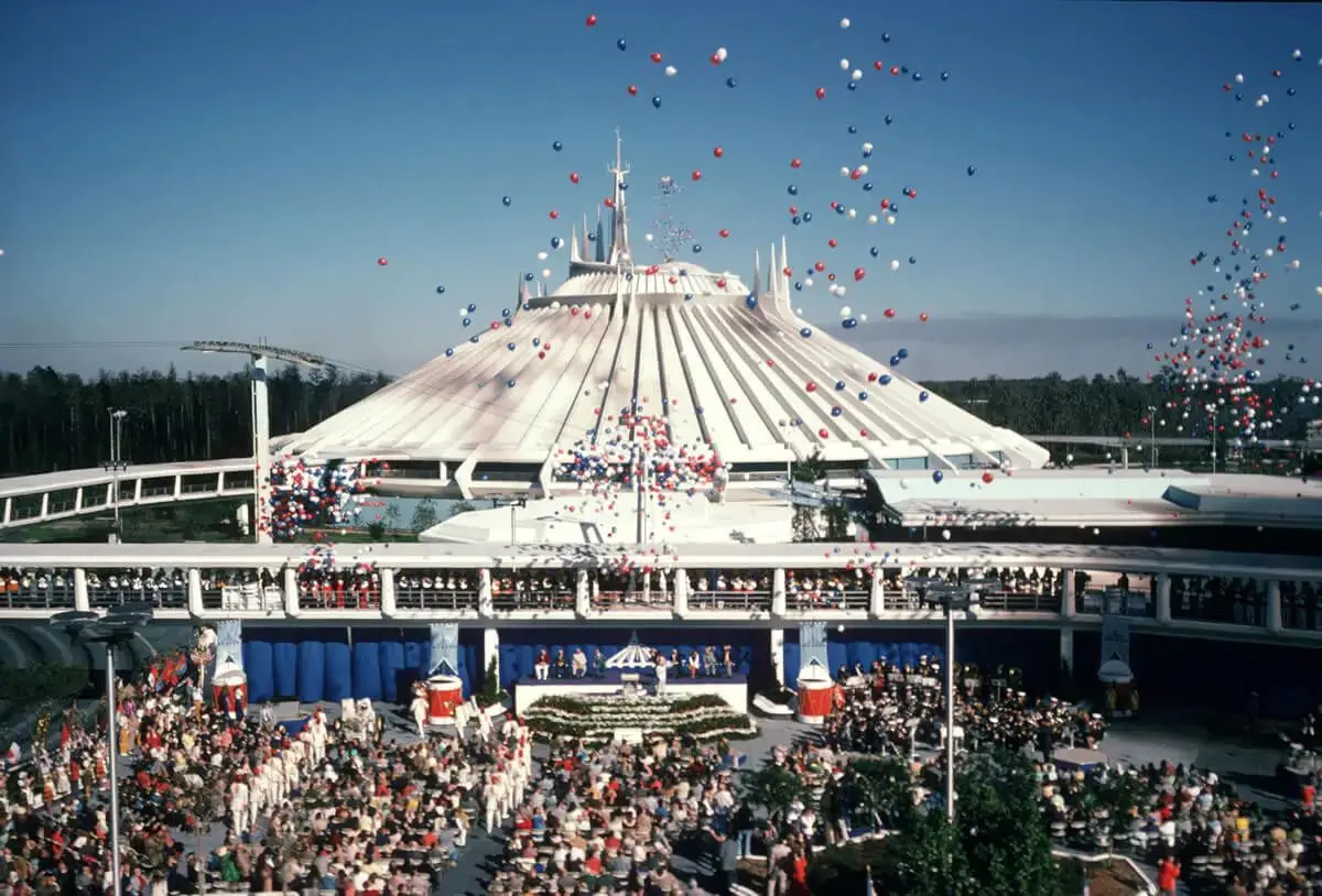 Historic opening day ceremony of Space Mountain at Walt Disney World’s Magic Kingdom, with a large crowd gathered in Tomorrowland and hundreds of red, white, and blue balloons released into the sky above the iconic white mountain-shaped structure.